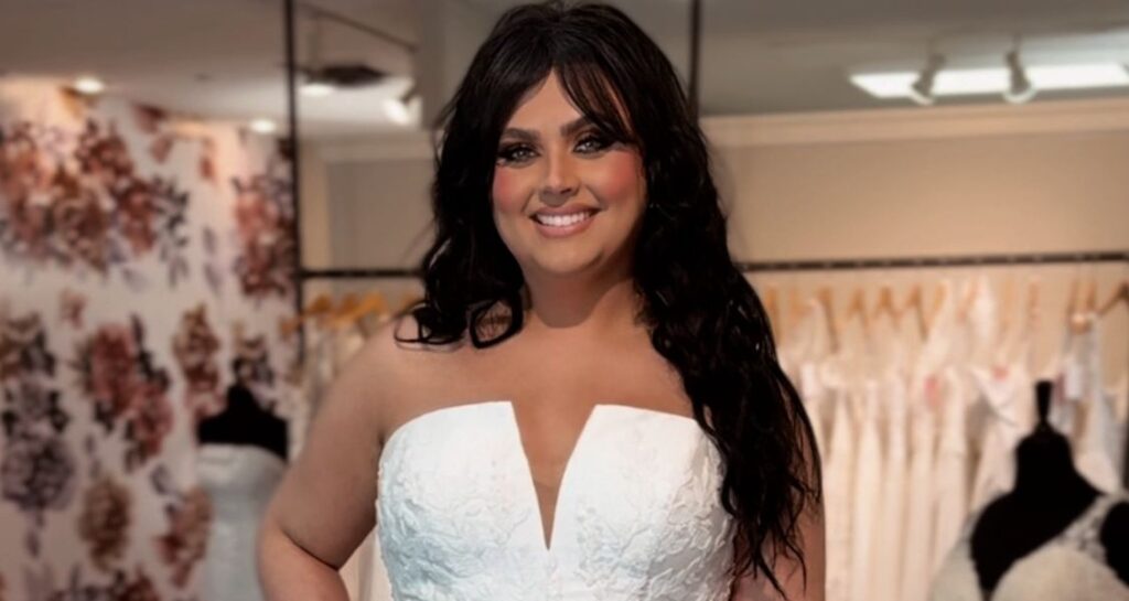 Bride smiling while trying on a strapless ballgown wedding dress with a deep V neckline and textured floral details at Amanda’s Touch.
