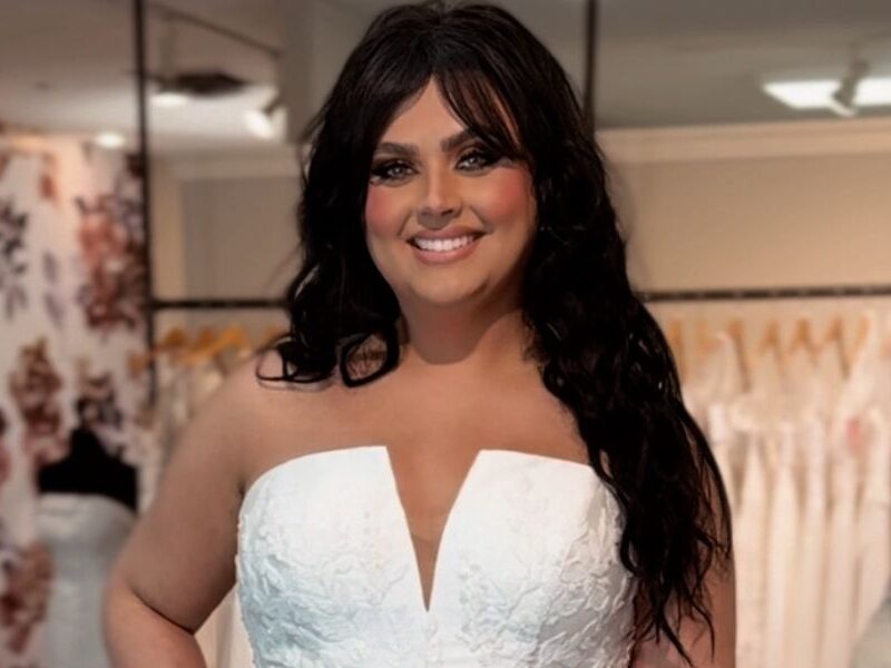 Bride smiling while trying on a strapless ballgown wedding dress with a deep V neckline and textured floral details at Amanda’s Touch.