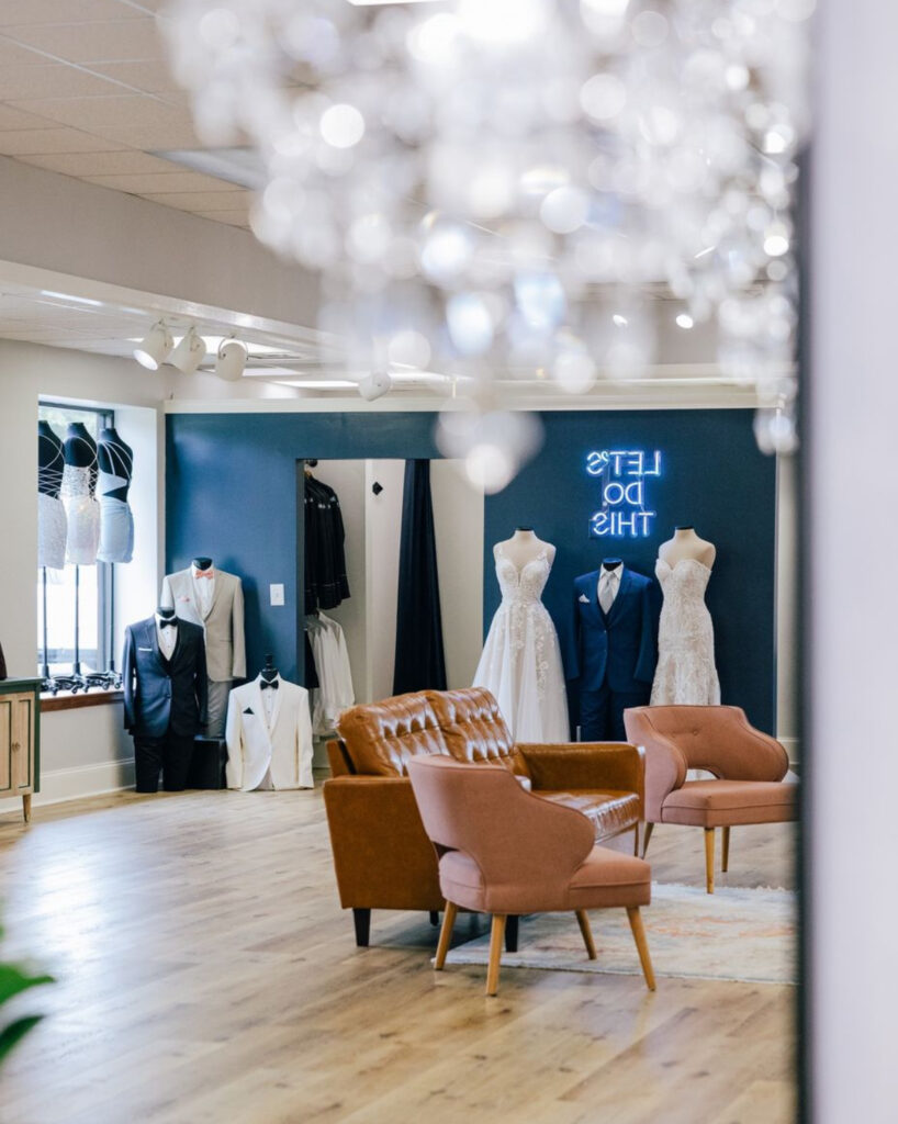 Inside of Amanda's Touch wedding dress store with a blue accent wall and suits and wedding dresses for sale.
