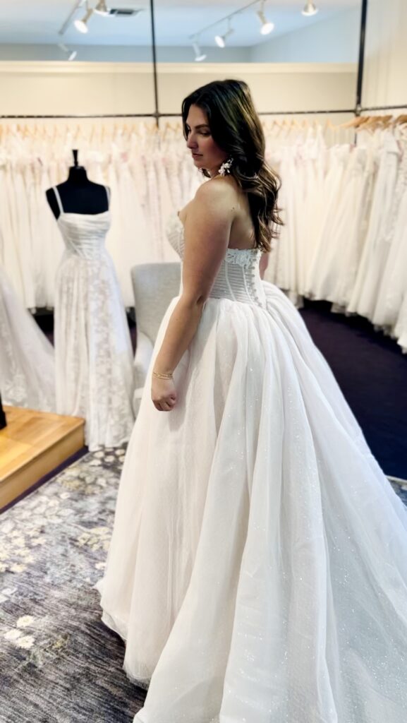 A bride wearing a corset basque waist wedding dress with subtle sparkle, looking down as the light catches the shimmer of her tulle skirt.