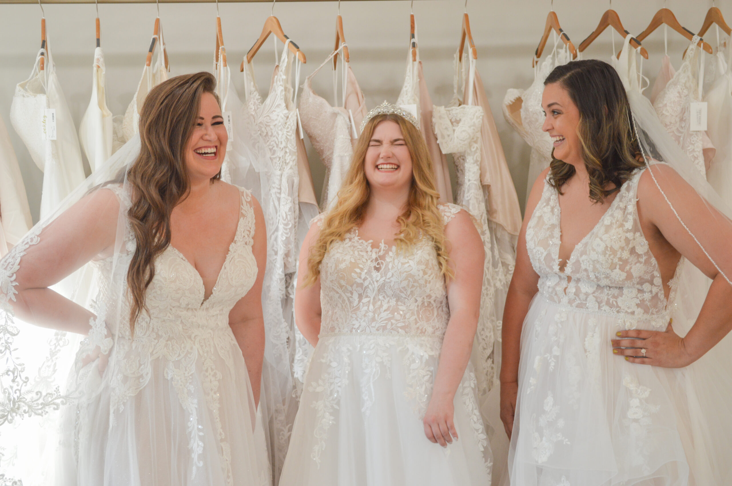3 brides in wedding dresses laughing in bridal store