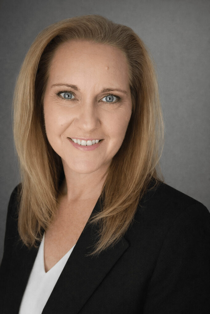 Professional headshot of Amanda Cash wearing a black blazer, smiling against a neutral gray backdrop.