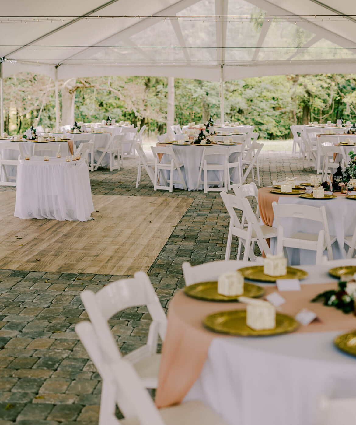 Wedding reception setup under a white tent with round tables, white chairs, and neutral-toned table settings.