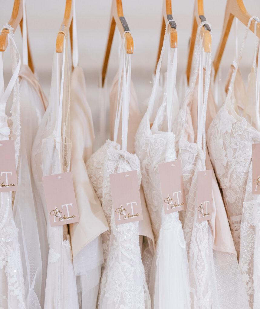 Close-up of wedding dresses hanging on wooden hangers with boutique tags attached.