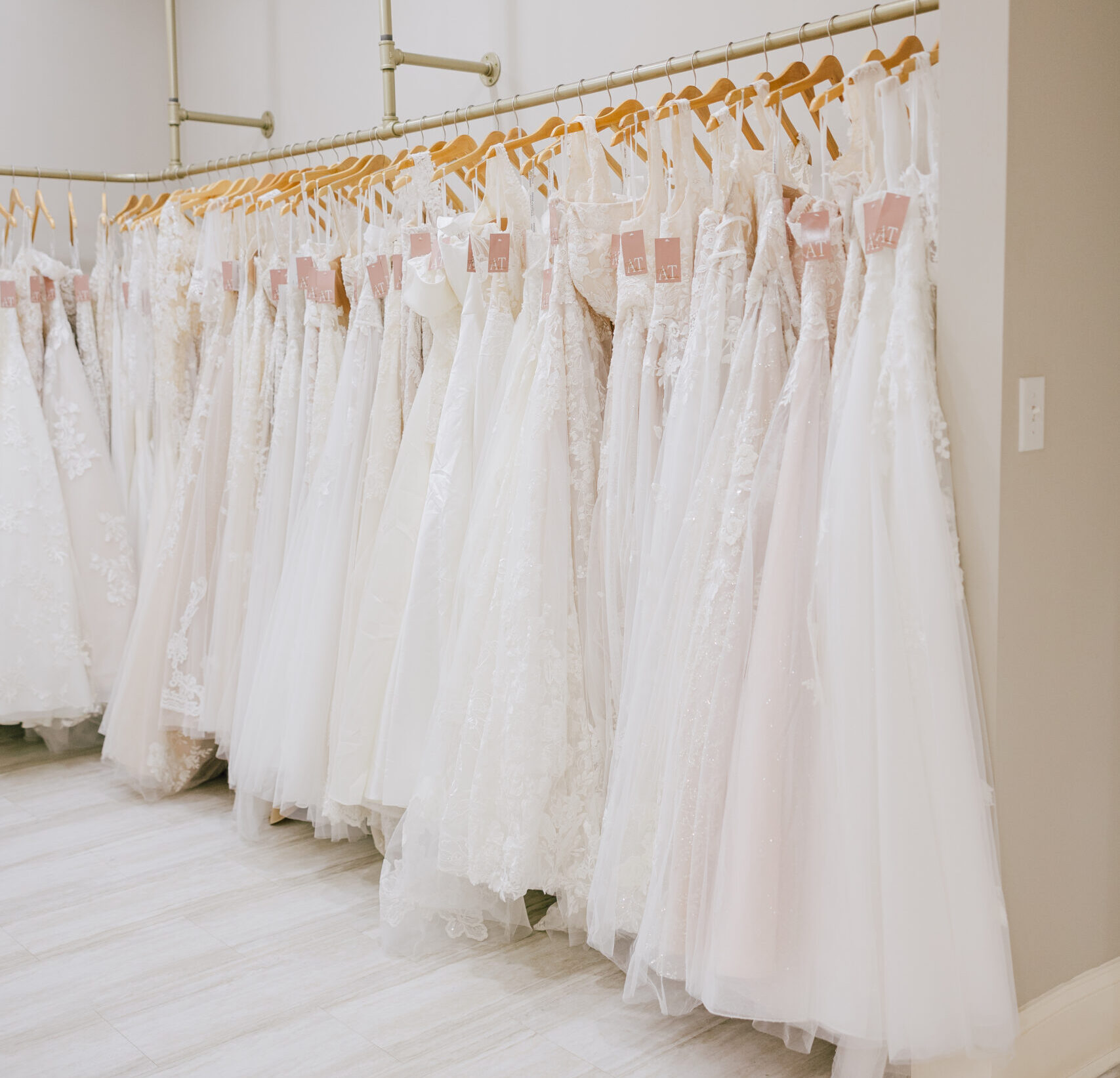 Long row of white wedding dresses hanging on racks inside a bright bridal boutique showroom.