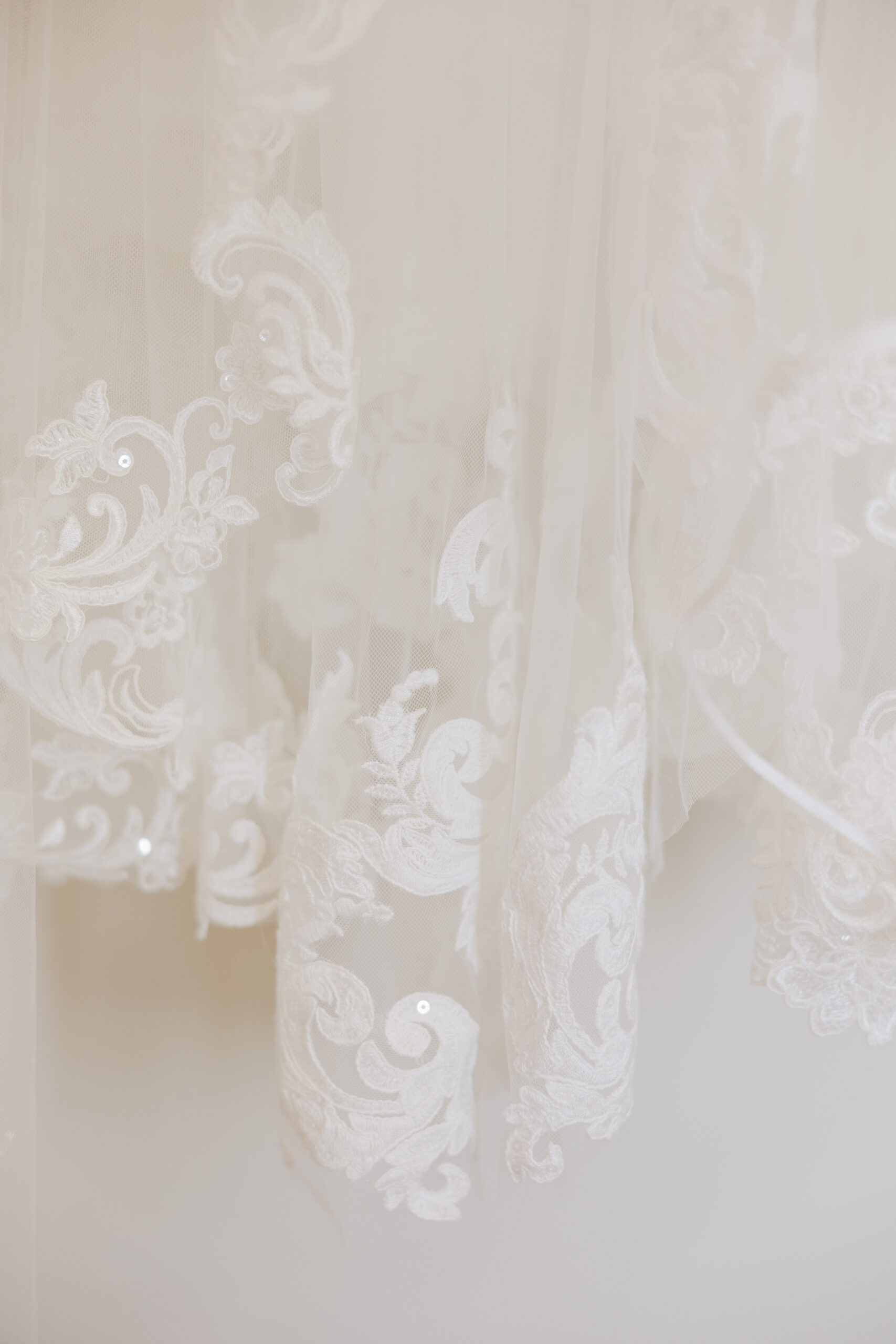 Close-up of white lace wedding dress fabric with embroidered floral detailing and sheer tulle layers.