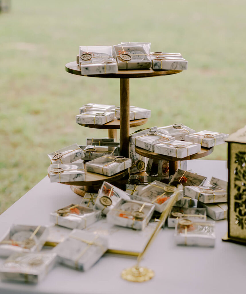 Wrapped wedding favors displayed on tiered wooden stands on a reception table with a blurred outdoor background.