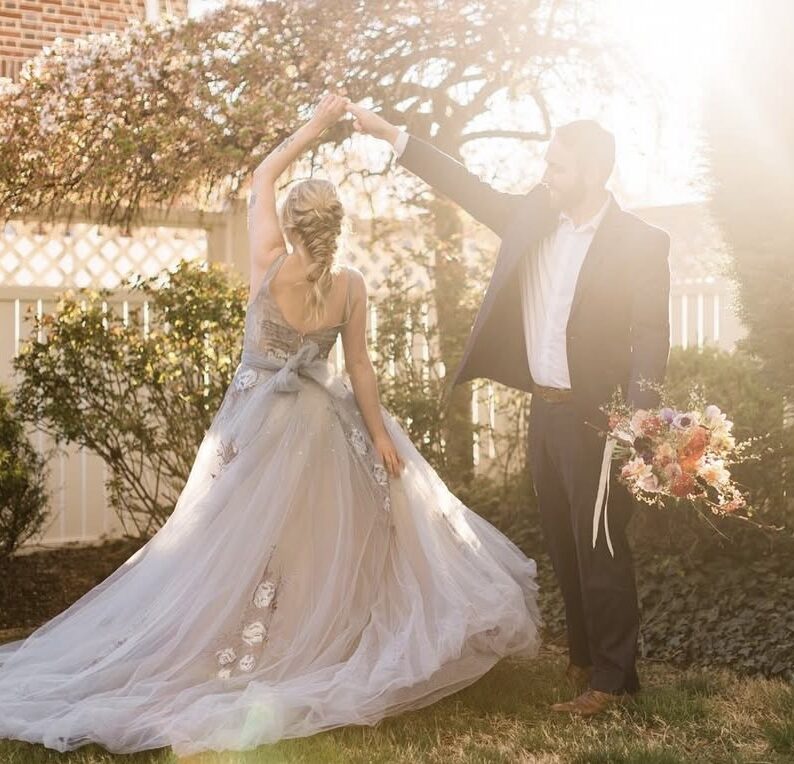 Groom twirling a bride in a flowing tulle wedding gown during an outdoor portrait session at sunset.