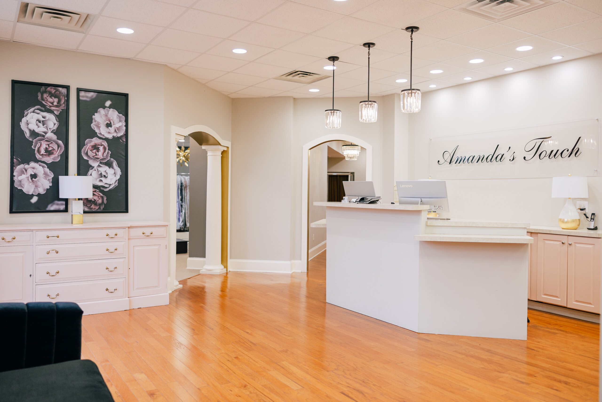 Bright bridal boutique reception area with front desk, floral wall art, pendant lights, and wood floors.