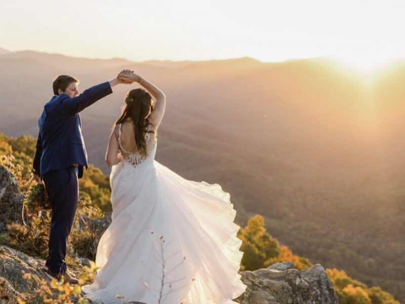Bride and groom standing on a rocky mountain overlook during sunset with rolling hills in the background.