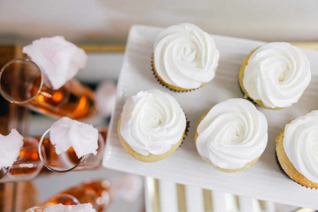 Close-up of frosted cupcakes and pink beverages topped with cotton candy on a serving display.