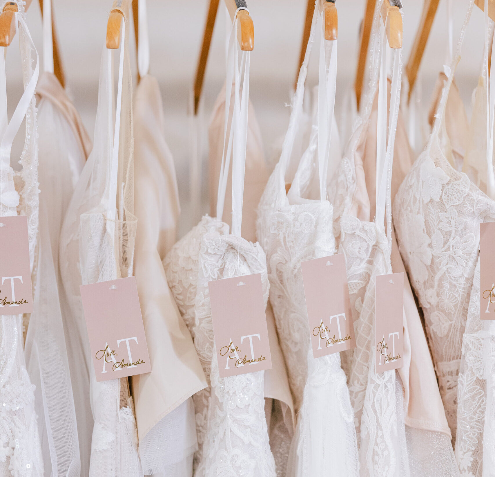 Close-up of lace and tulle wedding dresses hanging on wooden hangers inside a bridal boutique.