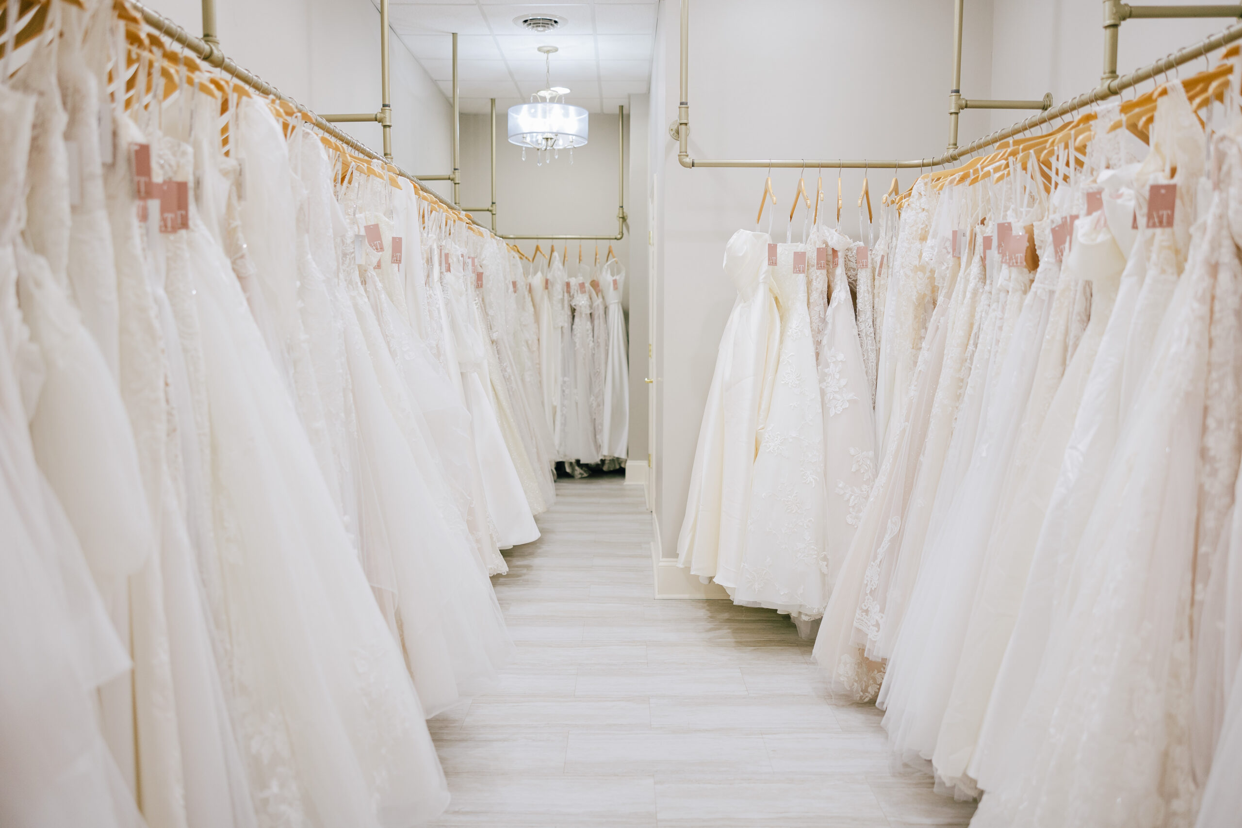 Rows of wedding dresses hanging on racks in a bright bridal boutique showroom.